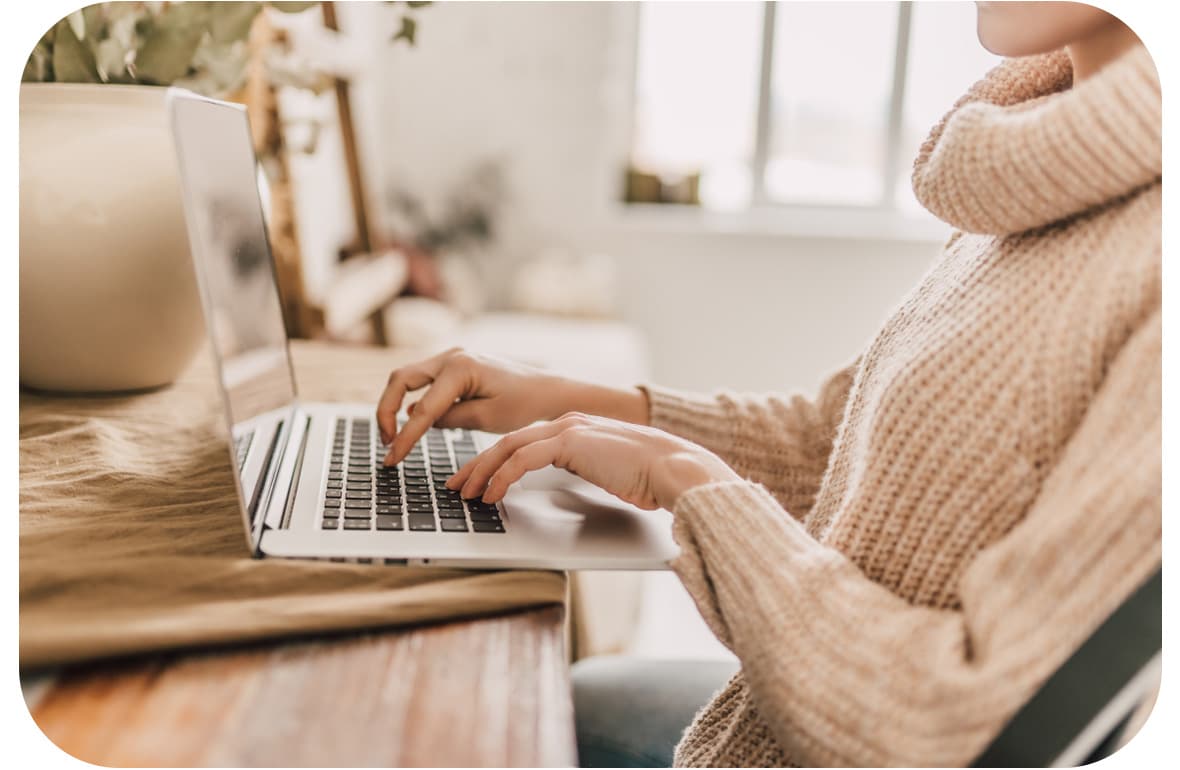 A caucasian woman is at her desk typing on her laptop.