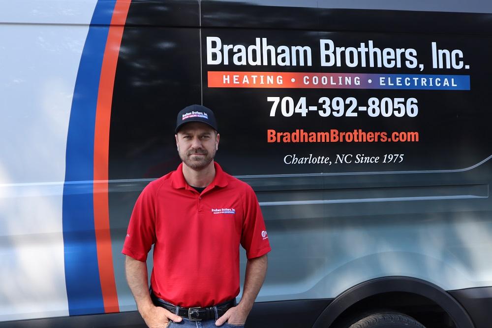 An HVAC technician is standing in front of his service truck.