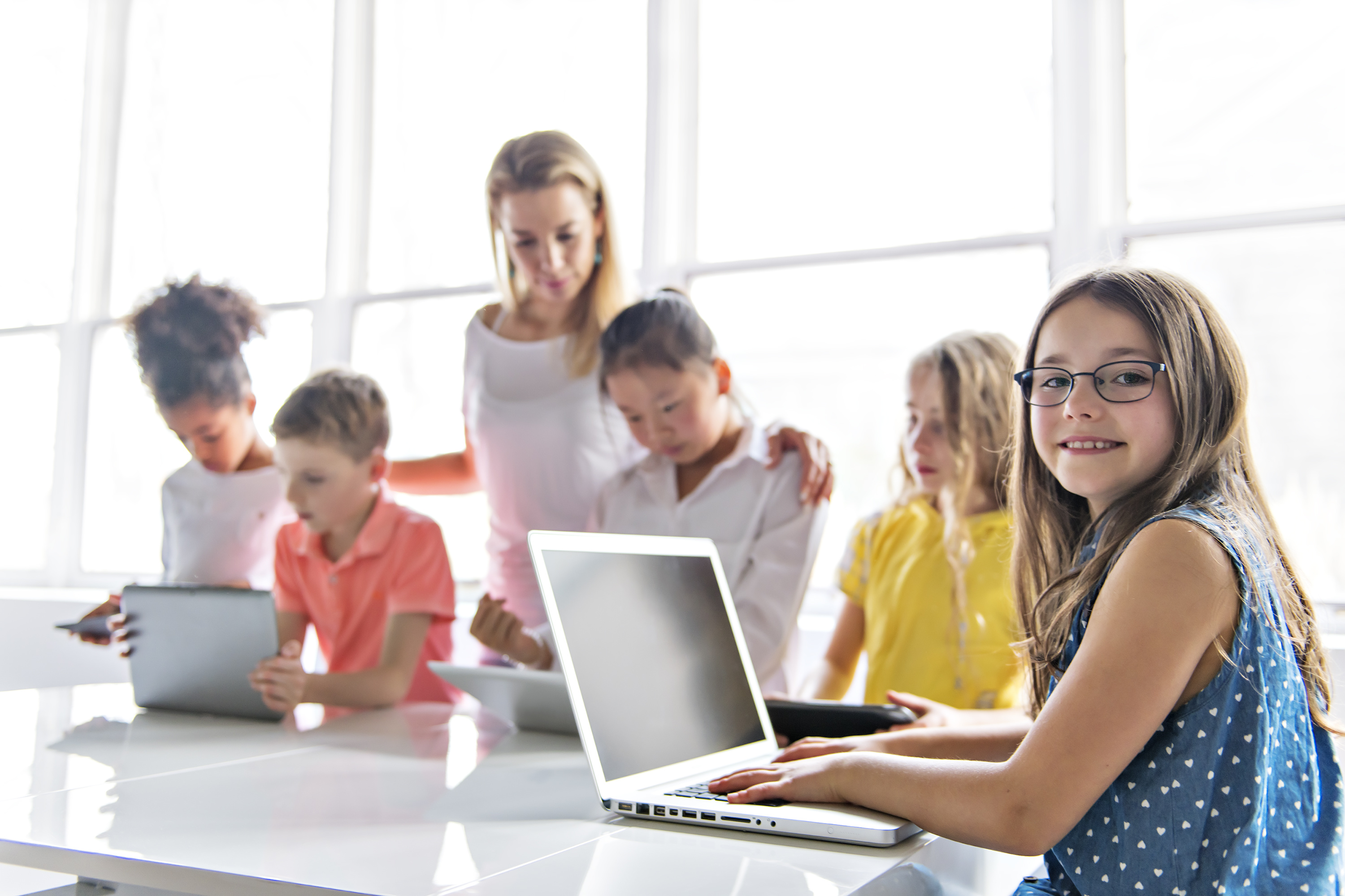 child with technology tablet and laptop computer in classroom teacher on the background