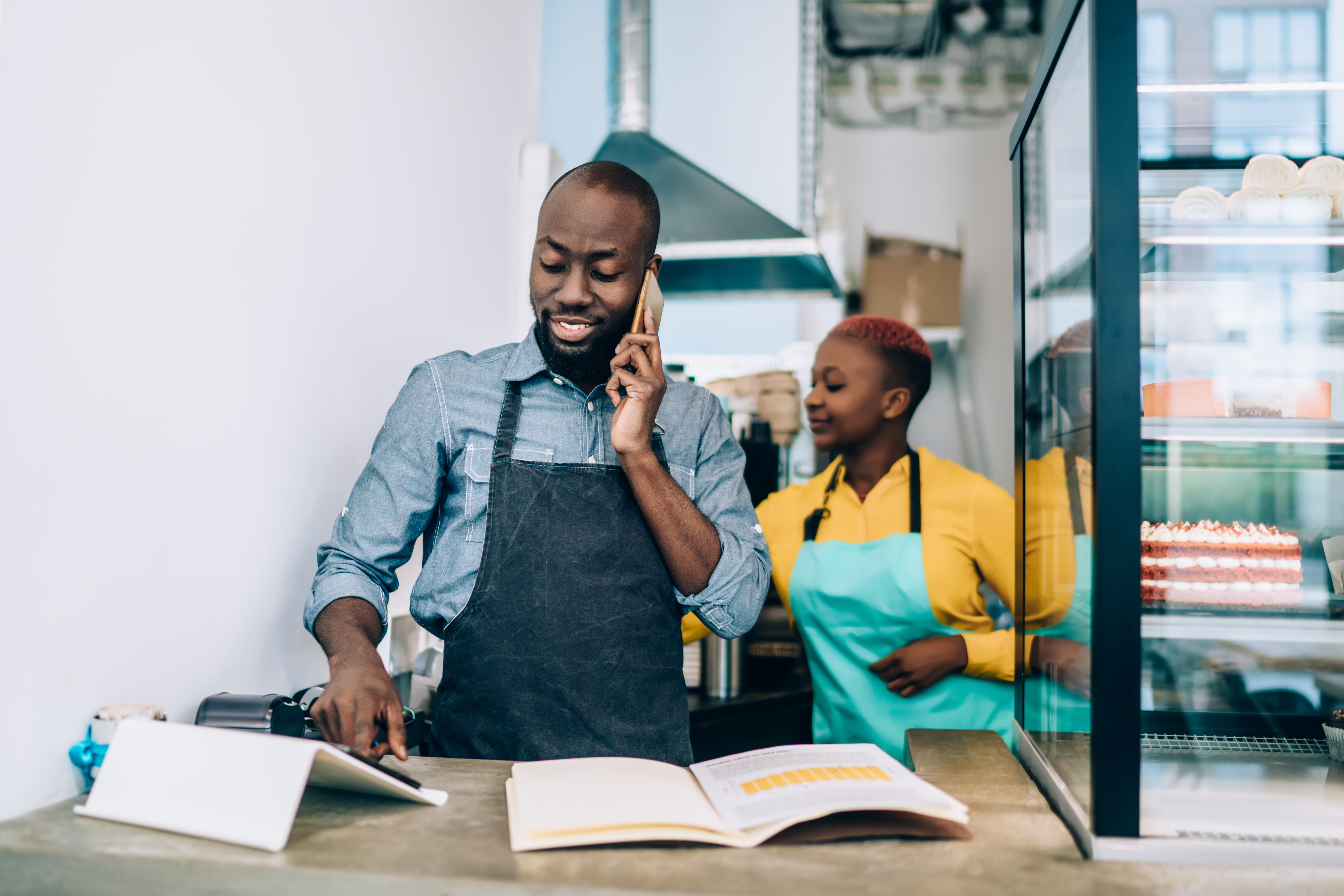 Owner of confectionery shop standing at counter and talking on phone