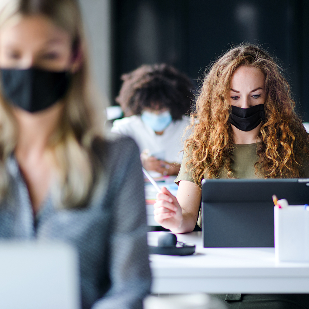 Young people with face masks back at work or school in office after lockdown.