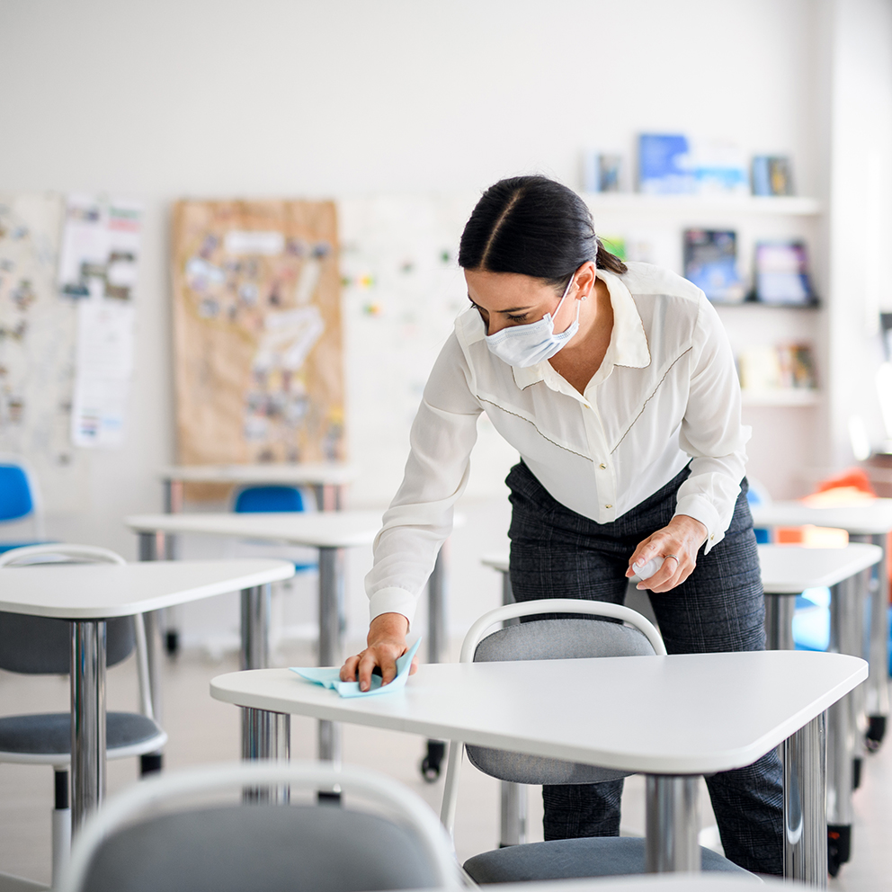 Teacher back at school after covid-19 quarantine and lockdown, disinfecting desks.